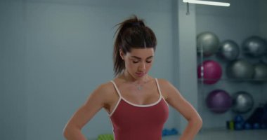 Kız sporcu, antrenman sırasında başını öne ve arkaya eğiyor. Egzersiz ekipmanlarıyla çevrili iyi aydınlatılmış bir spor salonunda tekniğine odaklanıyor..