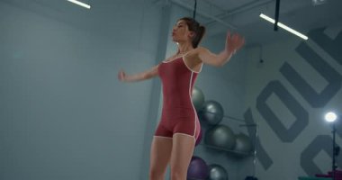 Kız sporcu, iyi donanımlı bir spor salonunda bir dizi zıplama hareketine katılıyor. Kararlılık ve odaklanma gösteriyor. Enerjik hareketlerle spor rutinini gösteriyor..