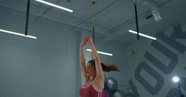 Modern bir fitness stüdyosunda atletik bir kız odaklanarak ve enerjiyle zıplama hareketleri yapıyor. Hareketleri coşkuyu ve fiziksel eğitime bağlılığı gösteriyor..