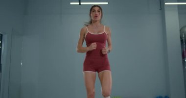 In a spacious indoor training facility a girl athlete engages in butt kicks enhancing her leg strength and agility. Her determination is evident as she works hard on her fitness routine.