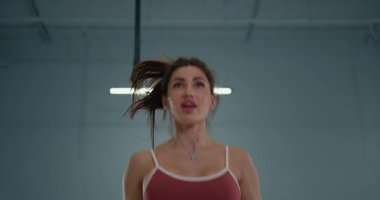 dedicated girl athlete executes butt kicks with focus and energy in an indoor gym. The late afternoon sunlight highlights her movement showcasing her commitment to fitness.