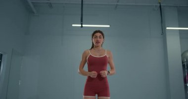 girl athlete performs butt kicks in a well lit gym. She wears athletic attire and shows focus and determination as she engages in her workout routine enhancing her fitness level and agility.