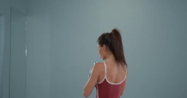 Spor salonunda bir kız sporcu diz çökme egzersizi yaparken tekniğine odaklanır. Yumuşak ışıklandırmayla çevre minimalistiktir..