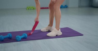 Kız sporcu spor salonundaki antrenmanına hazırlanıyor. Egzersiz rutinine odaklanıyor. Eğitimini arttırmak için bacaklarına lastik bant takıyor..
