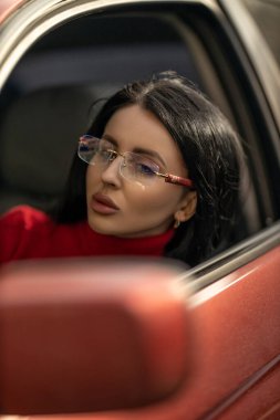 Gözlüklü güzel bir kız arabanın yolcu koltuğunda oturur. Düşünceli bir şekilde pencereden dışarı bakar. Gün ışığı yüzünü parlatır ve yüz hatlarını güçlendirir.