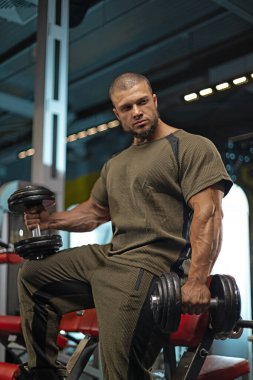 Erkek sporcu, iyi donanımlı bir spor salonunda dambılları kaldırırken dikkatle odaklanır.