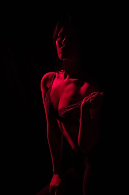 Model, kırmızı ışığın aydınlattığı karanlık bir ortamda kendine güvenen bir duruş sergiliyor, siluetini vurguluyor ve büyüleyici bir atmosfer yaratıyor.