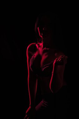 Model, bastırılmış ışıkta şık bir duruş sergiliyor, kırmızı tonlarla siluetini vurguluyor. Yaratıcı bir ortamda sanatsal, vurgulu bir hava var.