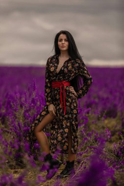 Güzel esmer, kendine güvenen, çiçek açan dehlizlerle dolu bir alanda duruyor. Bulutlu gökyüzü, bu dingin ortama dramatik bir dokunuş ekliyor. Etrafındaki canlı renkleri güçlendiriyor.