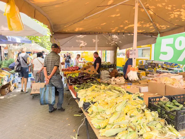 Ziyaretçiler, satıcıların UA Odesa Vladyslav Buwalkin St. 13 Temmuz 2025 'te mallarını sergiledikleri büyük çadırın altında taze meyve ve sebzelerle dolu canlı bir açık hava pazarı keşfediyorlar.