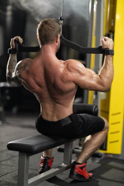 Kas sporcusu, sırt ve omuzlarını güçlendirmek için ön çekme egzersizi yapar. Spor salonu çeşitli ekipmanlara ve eğitim için odaklanmış bir atmosfere sahiptir..