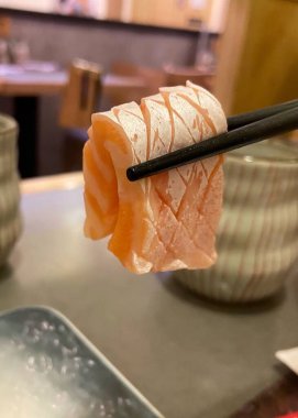 Sashimi, somon göbeğini kapat. Çubuklarla tut, Japon restoranının arka planında. 