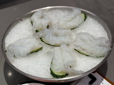 Paslanmaz çelik kasede buzun üzerinde çiğ karides, sıcak tencereye hazır.