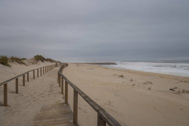 Costa Nova plajında rüzgarlı bir öğleden sonra Aveiro, kum tepelerinin yanındaki ahşap patika, okyanus esintisi, dalgalar