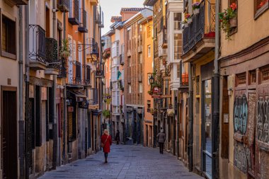 Vitoria-Gasteiz, İspanya - 26 Mart 2023: İnsanlar balkonlarında çiçeklerle renkli bir sokakta yürüyor