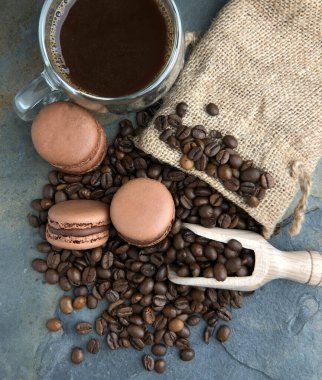 Kahve çekirdekleri, badem kurabiyeleri ve kahve. Gri taşlı arka planda bir çuval içinde. Tahta bir aletle.