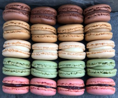 Kahverengi, bej, pembe ve yeşil renklerde 20 badem kurabiyesi üst üste dizilmiş, yukarıdan yakından çekilmiş.