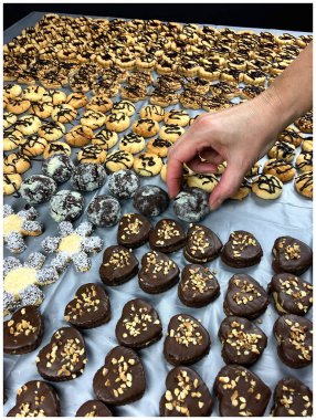 Büyük bir çikolata kaplı kurabiye çeşidi, bazıları fındıklı ve diğerleri sade; bir el sanatsal olarak dekore edilmiş bir kurabiyeyi almak için uzanıyor