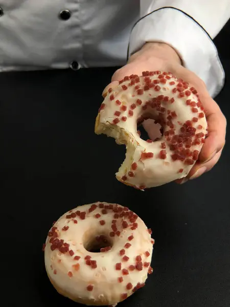 Bir şefin eli kırmızı şekerli donutu tutarken bir lokma masanın üstünde beyaz jöleli başka bir çöreğin yanında oturuyordu.