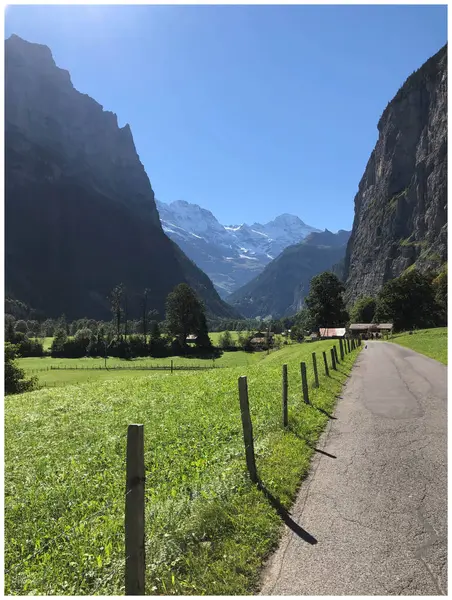 Lauterbrunnen Vadisi, İsviçre, açık mavi gökyüzü, arka planda dağlar, yeşil çayırlar, ve yol boyunca çitleri olan Lauterbrunnen Şelalesi 'ne giden bir yol, güneşli bir gün, yaz mevsimi