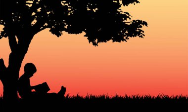 Küçük çocuk parkta ağacın altında kitap okuyor.