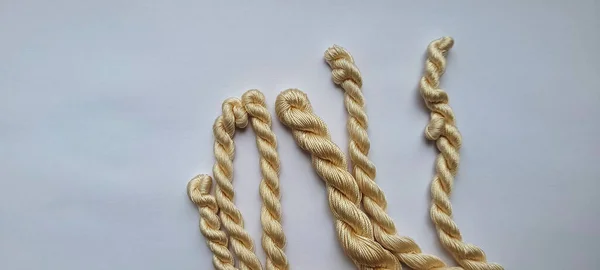 Beyaz arka planda ince ipek iplikler. İnce, doğal renkli ipekten bir demet, sıkıca birbirine dolanmış ve beyaz arka planda bir deste halinde dizilmiş. Örgü ve tığ işi için iplik. El sanatları için malzemeler.