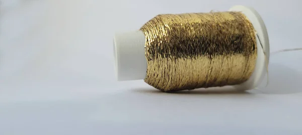 Altın rengi ince metalik lureks iplik. Beyaz arka planda işçilik yapmak için bir makara altın metalik iplik. Dekorasyon, nakış, örgü ya da örgü için ışıldayan iplik.