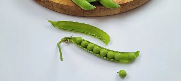 Pea pod with peas. Pisum sativum. Close-up of fresh, vibrant green pea pods bursting with young peas, beautifully arranged on a white background. These tender and nutritious legumes are a true summer delight