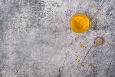 Gri arka plan deseni pürüzlü. Bir fincan çay, papatya çayı ve çay süzgeciyle. Uzayı kopyala en üstteki görünüm