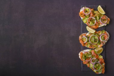 Açık sandviçler, tuzlu somon, krem peynir, soğan, kapari, salatalık ve mikroyeşillikler, koyu gri arka planda. Deniz ürünleri. Sağlıklı yiyecekler. Kapatın. Üst Manzara. Boşluğu kopyala