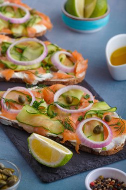 Tuzlu somon, krem peynir, soğan, kapari, salatalık ve mikroyeşillikli açık sandviçler beyaz mutfak masası arka planında. Deniz ürünleri. Sağlıklı yiyecekler. Kapatın. Boşluğu kopyala