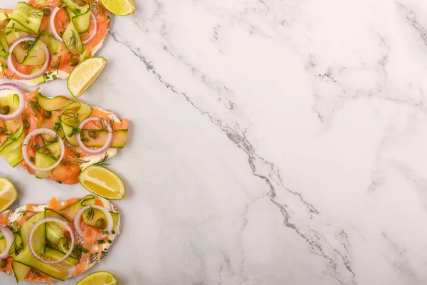 Tuzlu somon, krem peynir, soğan, kapari, salatalık ve mikroyeşillikli açık sandviçler beyaz mutfak masası arka planında. Deniz ürünleri. Sağlıklı yiyecekler. Kapatın. Üst Manzara. Boşluğu kopyala