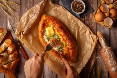 Bıçak ve çatalla kadın eli. Yumurta ve peynirle kesilmiş Khachapuri. Gürcistan ulusal yemeği. Üst görünüm