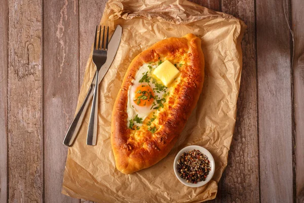 Geleneksel Gürcü yemeği khachapuri ajarian kırsal ahşap mutfak masası arka planında. Taze pişmiş Khachapuri. Peynirli ve çiğ yumurtalı Ulusal Gürcü hamur işleri. Üst görünüm