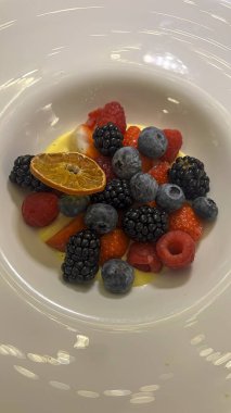 Çeşitli taze böğürtlen ve bir dilim canlı portakalla süslenmiş beyaz bir tabak.