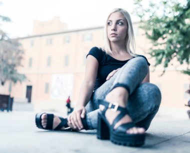 Elektrikli mavi kot pantolon giymiş mutlu bir kadın bacaklarını çapraz yapıp, seyahat maceralarına hazır bir şekilde yerde oturuyor. Flaşlı fotoğraf çekmeyin lütfen.