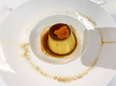 Lezzetli bir tatlı, canlı bir çiçek garnitürüyle beyaz bir tabakta zarif bir şekilde sergileniyor, güzel bir yemek ve bulaşık takımı sunumu sergileniyor.