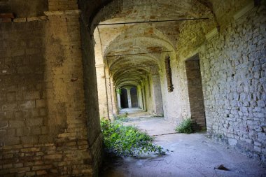 İçinde kemerler, tuğla duvarlar ve kırsal armatürlerin bulunduğu uzun koridorlu terk edilmiş bir bina. Ön cephe sarmaşıklarla kaplı, terk edilmiş eve bir parça sanat katıyor.