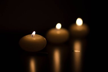 Gece yarısı yanıp sönen alevleriyle karanlık masayı aydınlatan üç mum. Ilık parıltı olay için yansıtıcı bir ortam yaratır.