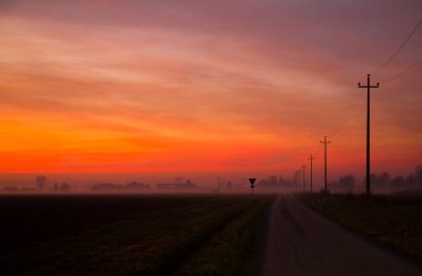 Resmedilmeye değer doğal bir manzara, ön planda elektrik hatları olan toprak bir yolun üzerinde gün batımını barındırır. Bu da, sabah kızıl bir gökyüzünün altında ekorejinin ardından güzel bir parıltı yaratır.