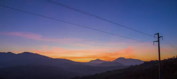 A hazy image capturing a red sky at morning with the silhouette of a mountain range and power lines in the foreground, creating a tranquil natural landscape