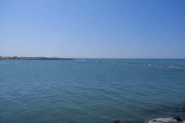 Güzel mavi gökyüzünün altında, sıvı, ufuk, bulutlar ve rüzgar dalgaları gibi elementlerle çarpıcı bir manzara yaratan görkemli bir su kütlesi.