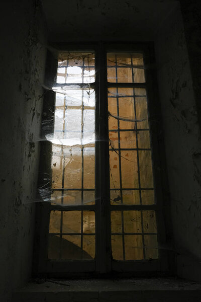 In a dimly lit room, a window allows a beam of light to filter through, casting shadows. The window is made of glass and is set within a composite material structure