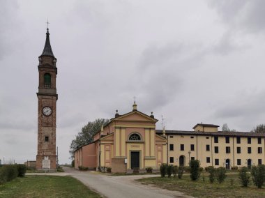 Geniş bir tarlanın ortasında bulunan bir saat kulesi olan bir kilise var. Etrafı açık gökyüzü, kabarık bulutlar ve resim gibi manzaralarla çevrili.