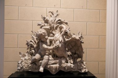 Tuğla duvarın önünde keçi tutan bir çocuk heykeli, metal ve ahşap elementlerle sanat ve görsel sanatları temsil eden güzel bir heykeldir.