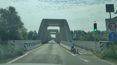 Güzel tasarlanmış kemerli bir köprü, yemyeşil ve parlak mavi gökyüzü tarafından çerçevelenmiş yoğun bir yol boyunca uzanır.
