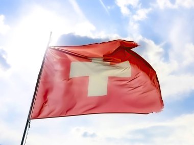 Belirgin bir beyaz haç bulunan canlı bir İsviçre bayrağı hafif esintide zarif bir şekilde dalgalanıyor.