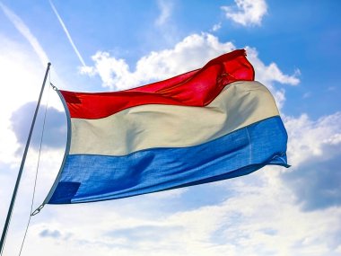 Güzel bir açık hava sahnesinde ulusal gururu sembolize eden, bulutlu bir gökyüzünde renkli Hollanda bayrağı dalgalanır.