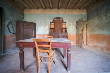 Boş bir odada, birkaç sandalyeyle çevrili basit bir masa var. Etrafında düzgünce düzenlenmiş, minimalist bir atmosfer yaratıyor.