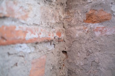 Kullanılan bazı materyalleri açığa çıkaran belirgin bir delik içeren dokulu tuğla duvarın detaylı bir yakın çekim görüntüsü.